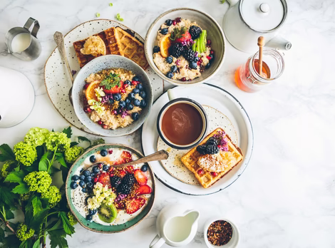 Großer Frühstückstisch mit Joghurt, Waffeln, Porridge, Honig & Milch 