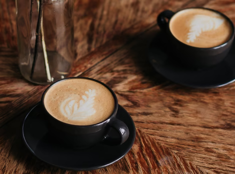 zwei Tassen Cappuccino auf einem Holztisch mit Schleierkraut Deko